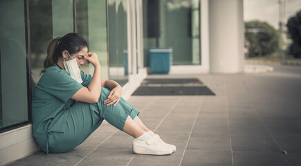 Tired depressed female asian scrub nurse wears face mask blue uniform sits on hospital floor,Young woman doctor stressed from hard work