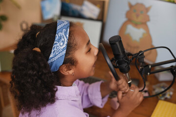 Side view closeup of young black girl speaking to microphone at home recording podcast for social media