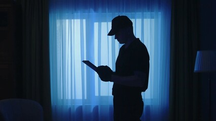 Closeup shot of policeman with tablet in the dark room, looking around, writing something. Crime scene creative concept.