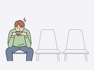 Sad man is waiting for start of interview, sitting in office corridor with empty chairs. Guy is nervous before interview because of problems in labor market and difficulty of finding well-paid job