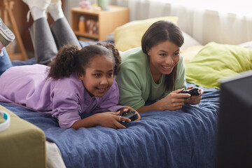 Portrait of happy teen girl playing videogames with mother at home and having fun together holding controllers © Seventyfour