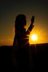 silhouette of a woman standing in front of the sun holding up her hand