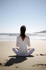 Fototapeta na wymiar rearview shot of a young woman meditating at the beach
