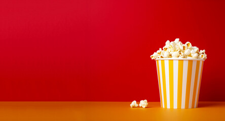 Popcorn box on the red and orange background. Popcorn in a bright glass. Popcorn minimal backdrop. Cinema concept. Banner for design. Snack food. Big yellow white strip box.  AI generated