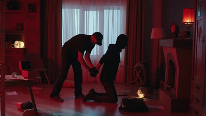 The arrest of the robber in a dark apartment, lit with red light. Side view of a criminal kneeling...