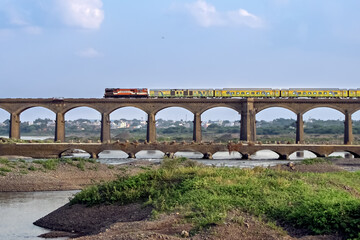 Fototapeta na wymiar On its inaugural run, super-fast Duronto express train crossing an old stone arc bridge in Daund, Maharashtra, India