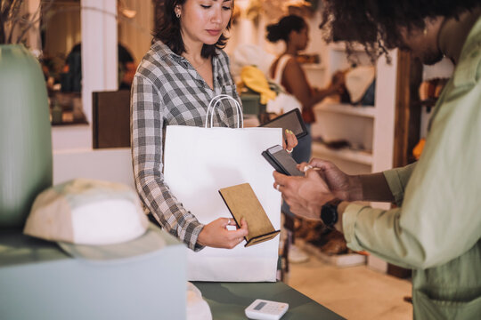 Young male customer scanning QR code through smart phone held by saleswoman at clothing store