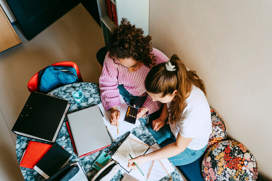 High angle view of young female friends using smart phone's calculator while homework