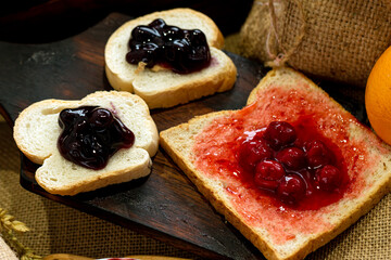 Three Slices of Baked Bread with Sweet Strawberry and Blueberry Jam on rustic wooden board; Homemade Breakfast Delight