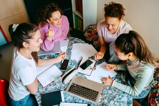 High angle view of female friends discussing while studying together at home