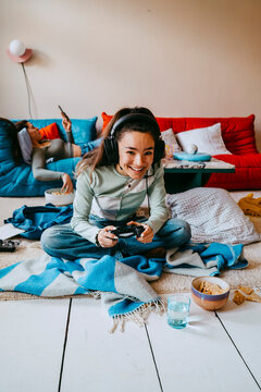 Young woman playing video game while friend using smart phone on sofa at home