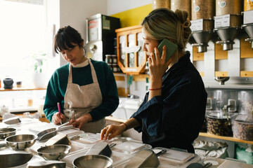 Owner talking on smart phone while colleague taking inventory in store