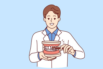 Man dentist explaining rules of brushing teeth, holding toothbrush and giant jaw in hands. Guy dentist recommends observing hygiene requirements to avoid appearance of caries in mouth