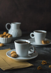 Two cups of coffee, a milk jug and cookies and an envelope on a dark background.