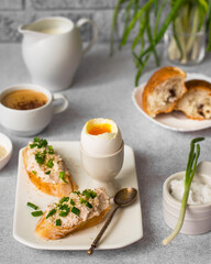 An example of a European breakfast with a sandwich with cream cheese, pate and green onions, egg, a cup of coffee, a milk jug and a croissant