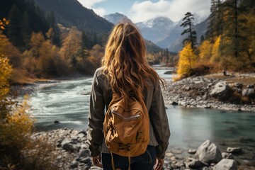 Back view of girl traveler with a backpack looking at a beautiful mountain river