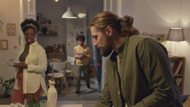 Tilt up shot of Caucasian man putting forks and knives on festive table while other family members preparing for family dinner