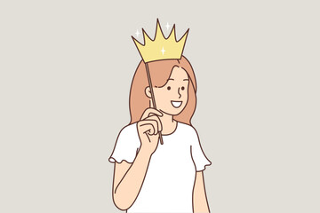 Teenage girl puts fake crown to head and smiles, dreaming of becoming princess or queen