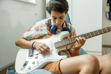 Chica adolescente haciendo un punteo en su guitarra eléctrica blanca en la habitación de su casa