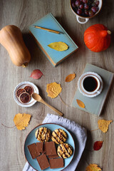 Cup of tea or coffee, plate with cookies and chocolate, dried oranges, bowl of grapes, vintage books, pumpkins and autumn leaves on the table. Autumnal hygge. Top view.