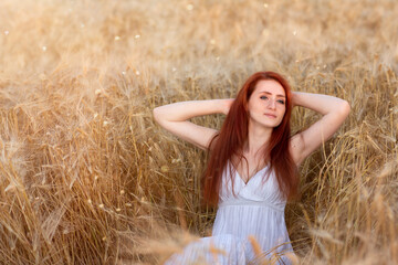 a redhead in a long white dress walks through a wheat field. The concept of a wedding and a walk in nature. red-haired girl in a field of wheat in a white dress smiles a lovely smile , a perfect pictu