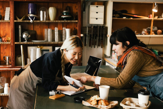 Multiracial female coworkers discussing over diary at upcycling workshop