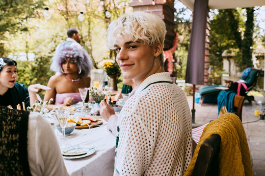 Portrait of smiling gay man with gray hair sitting amidst friends during dinner party in back yard