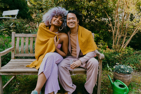 Portrait of smiling LGBTQ friends sitting together on bench during dinner party in back yard