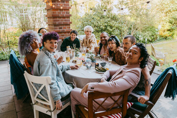 Portrait of happy friends from LGBTQ community sitting at dining table during dinner party in back yard