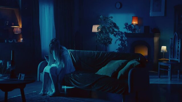 Video of a young woman sitting on the couch, staggering, with her head down and her arms dropped to the ground as if she is posessed by a ghost, demon, poltergeist.