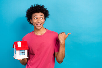 Portrait of impressed guy dressed stylish t-shirt hold small house directing empty space...