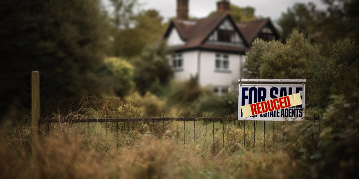 A for sale sign outside a house in England with a price reduced label on it, dropping house prices, reduction in price on the housing market