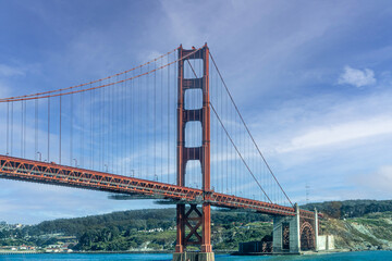 Fototapeta na wymiar San Francisco, CA, USA - July 13, 2023: Golden Gate bridge south landing , ocean side, with 1 tower under blue cloudscape. Green hills and city on horizon