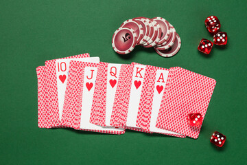 Poker chips, playing cards and dice on a green background. Top view. Royal flush, hearts suit....