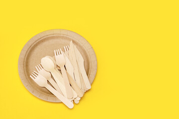 wooden disposable cutlery on a disposable paper plate on a yellow background with copy space