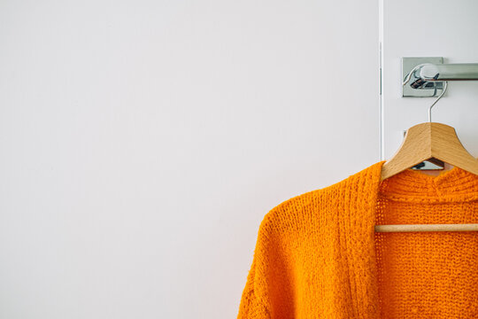 Autumn fall minimalist wardrobe with orange warm knitted sweater on wooden clothes hanger. Autumn capsule, warm fashion trends and stylish warm background, knitwear, copy space.