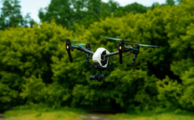 White drone over the forest. Dron against the cloudy sky. The flight of the copter in the sky