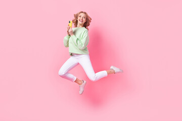 Fototapeta na wymiar Full length photo of energetic cheerful person jumping use smart phone empty space isolated on pink color background