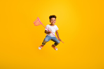Fototapeta na wymiar Full length photo of cheerful sweet little boy dressed white t-shirt jumping high catching butterflies isolated yellow color background