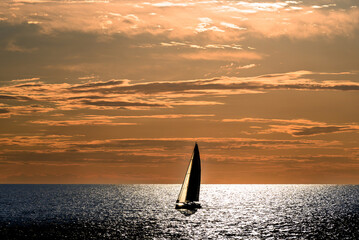 View of a sailing boat at sunset passing in front of the Artruxt Lighthouse, Cuidadela, Menorca, Balearic Islands, Spain	
