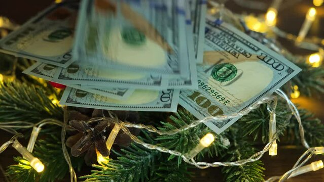Hundred-dollar bills fall on a Christmas tree with a garland. Money and Christmas