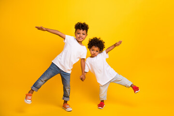 Fototapeta na wymiar Full size photo of two small funky carefree people hold arms have fun dancing isolated on yellow color background