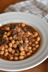 white plate of chickpeas with mushrooms and checkered cloth on wooden background