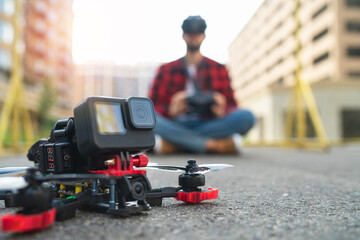 Close up cropped shot shot of generic desing fpv drone after landing on a street road, with male pilot on the background - 644174483