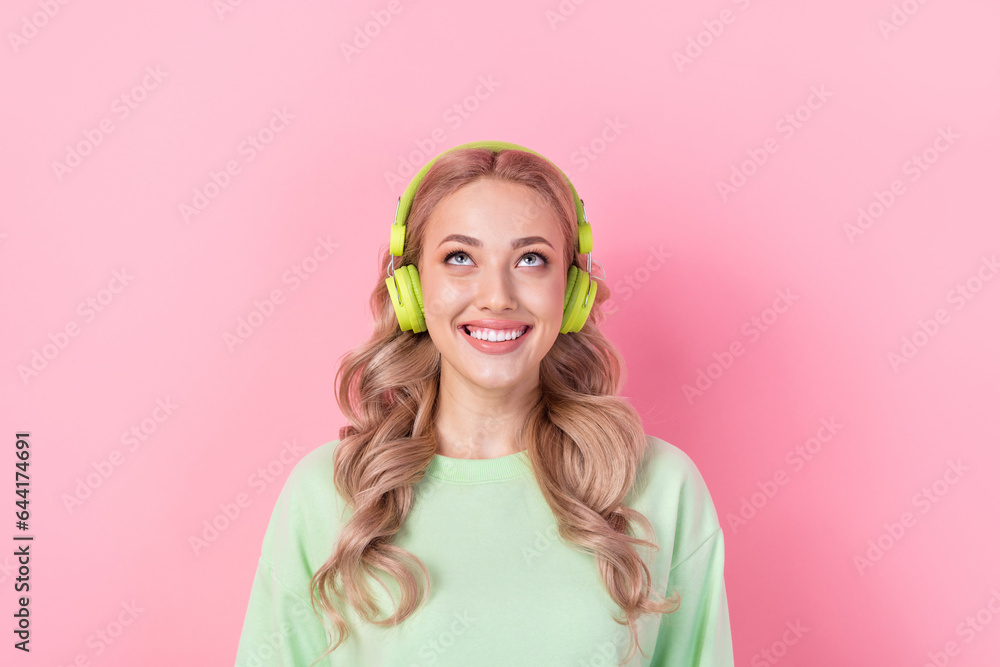 Wall mural Portrait of nice millennial girl blonde curls listen earphones dreaming looking above her head gadgets ad isolated on pink color background