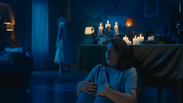 Shot of a young woman sitting, hiding behind the table from from an otherwordly creature, entity, ghost. Woman is frigtened, afraid to be noticed.