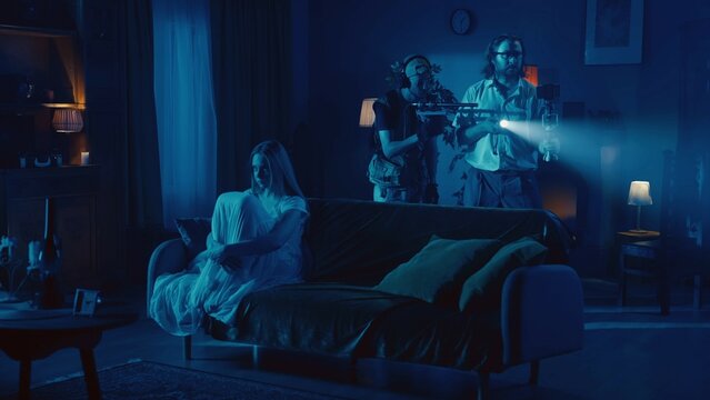 Shot of two ghost hunters looking for signs of paranormal activity, when there is a posessed female, ghost, poltergeist sitting on the couch right next to them.