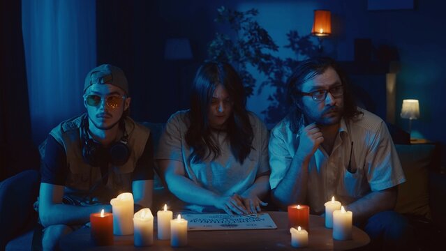 Shot Capturing A Group Of People Having An Ouija Board Session, Seance. Two Young Men Look Bored And Distrustful, Looking To The Sides, A Woman