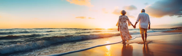 Foto auf Acrylglas Senior couple walking along a beach in the sunset. Concept of retirement, mature love and travel. Shallow field of view with copy space. © henjon