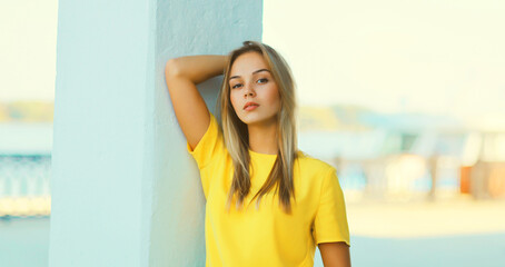 Portrait of stylish caucasian blonde young woman model posing in yellow t-shirt in the city